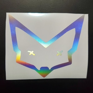 May include: A holographic sticker of a fox with an outline of a fox head. The fox has an iridescent rainbow color scheme and has an X for eyes.