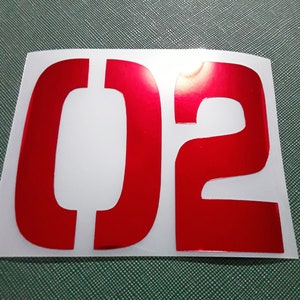 May include: Red vinyl number "02" with a glossy finish.
