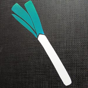 May include: A white and green paper cutout of a leek, a type of onion, on a black textured background.