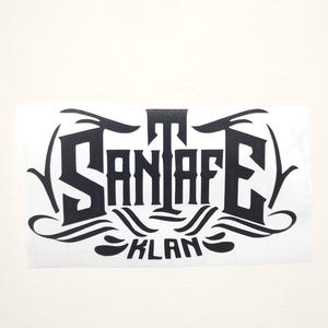 May include: Black and white graphic design with the text "Santa Fe Klan" in a stylized font.