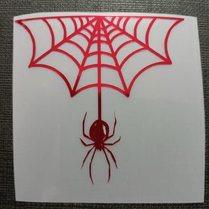 May include: A red spider web design with a spider hanging below. The spider and web are red and the background is white. The design is on a square sticker.