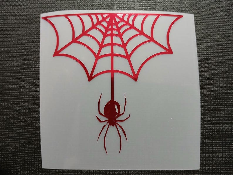 May include: A red spider web design with a spider hanging below. The spider and web are red and the background is white. The design is on a square sticker.