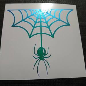 May include: A white sticker featuring a teal and green spider web design with a hanging spider. The spider and web have a gradient effect, transitioning from teal to green and purple. The sticker is square-shaped.