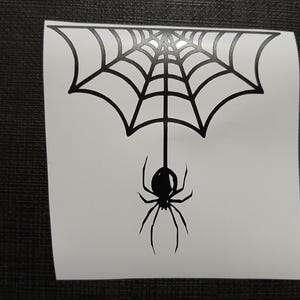 May include: Black spider and web design. The spider is hanging from the web. The web is a semi-circle shape. The spider has eight legs and a round body. The design is on a white background.