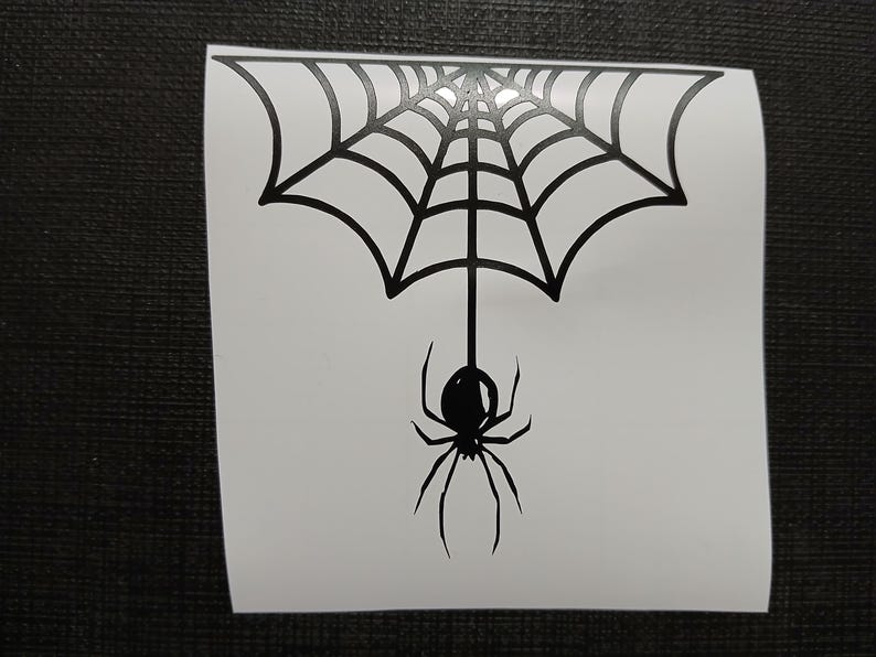 May include: Black spider and web design. The spider is hanging from the web. The web is a semi-circle shape. The spider has eight legs and a round body. The design is on a white background.