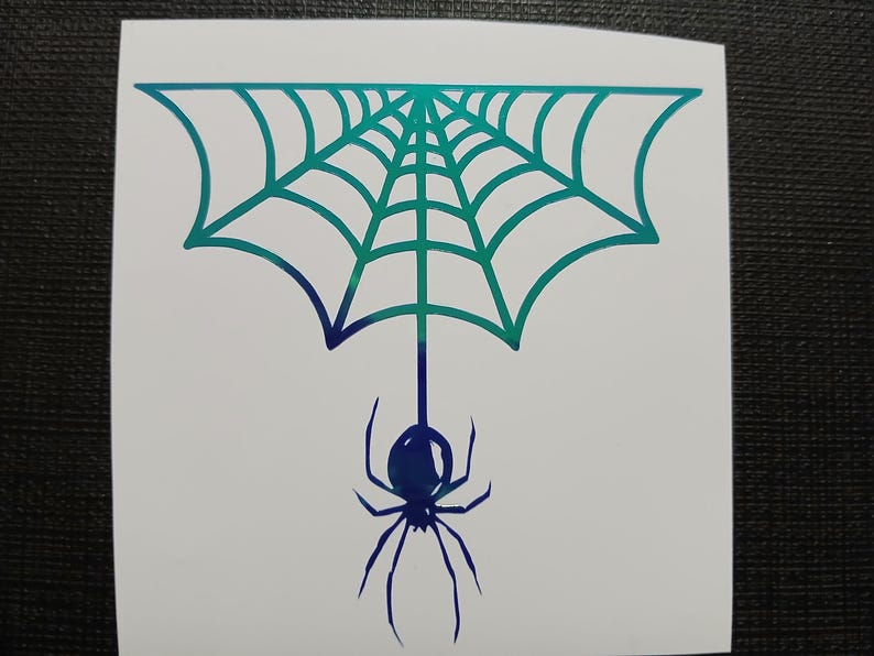 May include: A white sticker featuring a teal and blue gradient spider web design with a spider hanging below. The spider and web are outlined in a gradient of teal and blue.