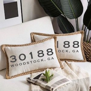 May include: Two decorative throw pillows with a beige linen fabric and brown trim. The pillows feature black text that reads "30188 WOODSTOCK, GA" and "188 OCK, GA".