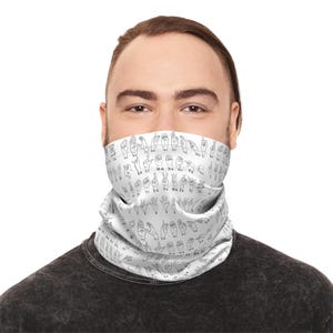 May include: A white neck gaiter featuring a black line drawing of the American Sign Language alphabet. The neck gaiter is wrapped around the lower face of a person. The background is white.