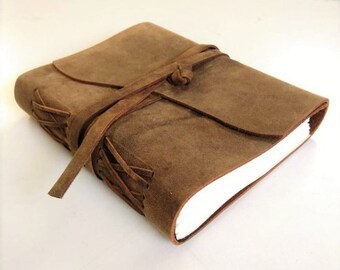 May include: A brown leather journal with a strap closure and a decorative lacing detail. The journal is closed and lying on a white surface.