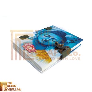May include: A blue and yellow journal with a painting of Buddha on the cover. The journal has a leather strap closure with a metal clasp. The text "The Retro Craft Co. Crafted with Love" is printed on the bottom right corner of the cover.