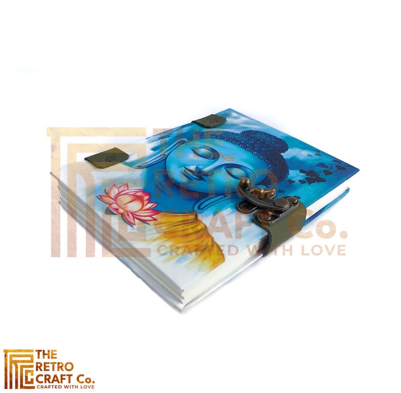 May include: A blue and yellow journal with a painting of Buddha on the cover. The journal has a leather strap closure with a metal clasp. The text "The Retro Craft Co. Crafted with Love" is printed on the bottom right corner of the cover.