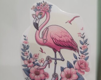 May include: A pink flamingo sticker wearing sunglasses, a flower crown, and a pearl necklace. The flamingo is adorned with high-heeled shoes and surrounded by pink flowers and blue leaves. A small bird is also depicted.
