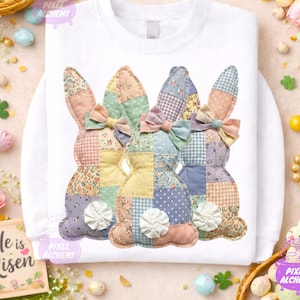 May include: White sweatshirt featuring a patchwork design of three Easter bunny silhouettes. Each bunny has a different patterned ear and body, with pastel colors and bow accents. The text "He is Risen" is visible on the left.