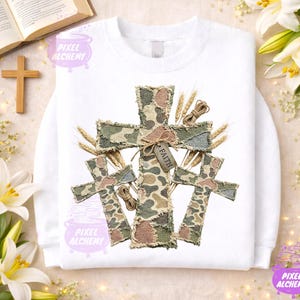 Könnte beinhalten: Weißes Sweatshirt mit einem Tarnmuster-Kreuz-Design und einem "Faith"-Anhänger. Das Design beinhaltet Weizenähren und Bindfäden, was eine rustikale, religiöse Ästhetik erzeugt.