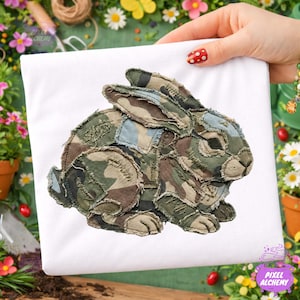 May include: White t-shirt featuring a patchwork rabbit design in camouflage colors of green, brown, and blue. The rabbit is centered on the shirt, with a detailed, textured appearance. The design is likely an applique or embroidered element.