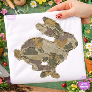 May include: A white t-shirt featuring a running rabbit applique. The rabbit is made of camouflage fabric in shades of green, brown, and tan. The edges of the applique are frayed. The text "PIXEL ALCHEMY" is visible in the lower left and right corners.