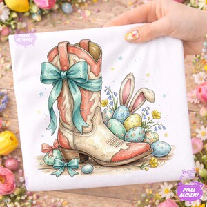 May include: White t-shirt featuring a watercolor illustration of a cowboy boot with a teal bow, Easter eggs, and bunny ears. The boot is cream, coral, and tan. The eggs are pastel colors with floral patterns. The design has a spring or Easter theme.