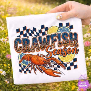 Puede incluir: Camiseta blanca con un gráfico colorido que dice "CRAWFISH Season". El diseño incluye un cangrejo rojo, rodajas de limón y un patrón de cuadros azules y negros. El texto tiene un diseño de estampado de leopardo.