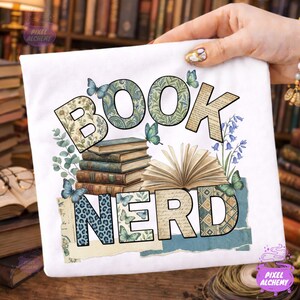 May include: White t-shirt with the words "BOOK NERD" in a decorative font. The design includes stacks of books, open books, butterflies, and floral elements in shades of green, blue, and beige.