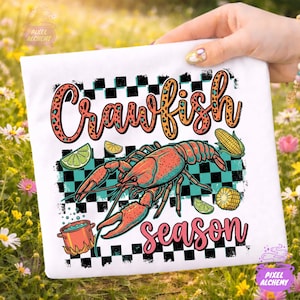 Può includere: Maglietta bianca con un design grafico colorato. Il design include le parole "Crawfish Season", un'illustrazione di un gambero di fiume ed elementi alimentari come mais e lime. Lo sfondo ha un motivo a scacchi neri e turchese.