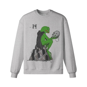 May include: A light grey sweatshirt with a green frog-like character in a black cape, holding a mask. The frog sits on a stone structure. The text "-II" is above the frog.