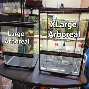 May include: Two black glass terrariums with black metal frames. The smaller terrarium is labeled "Large Arboreal" and the larger terrarium is labeled "XLarge Arboreal".