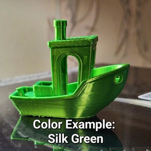 May include: A small green 3D printed model of a boat with a chimney. The boat is sitting on a black surface. Color Example: Silk Green