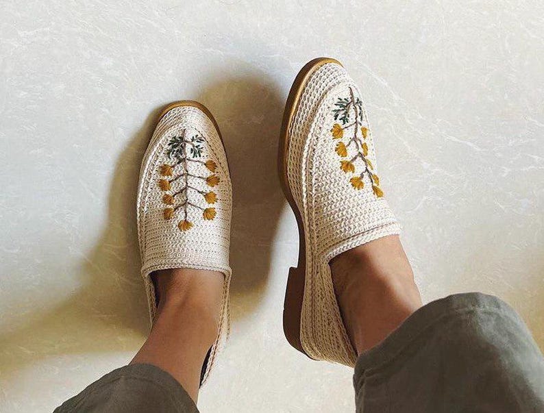 May include: Two white crocheted slip-on shoes with yellow and green embroidered floral designs.