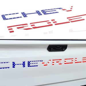 May include: A white truck tailgate with a red, white, and blue American flag design "CHEVROLET" emblem.