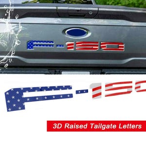 Puede incluir: Letras de port&oacute;n trasero 3D en relieve para un cami&oacute;n, con las letras "F-150". La "F" es azul con estrellas blancas, y el "150" es de rayas rojas y blancas, que se asemeja a la bandera estadounidense.