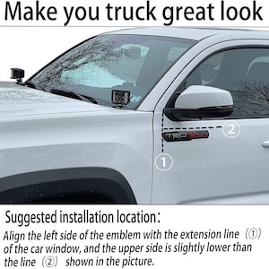 Puede incluir: Un cami&oacute;n blanco con un emblema negro "TRD OFF ROAD" en el lateral. La imagen muestra la ubicaci&oacute;n de instalaci&oacute;n sugerida para un accesorio de cami&oacute;n, con dos l&iacute;neas numeradas que indican los puntos de alineaci&oacute;n.