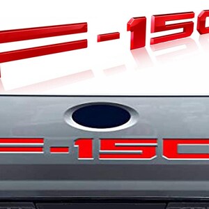 Puede incluir: Emblema rojo F-150, con las letras y n&uacute;meros en estilo 3D. El emblema se muestra en dos vistas diferentes, una con las letras y n&uacute;meros separados y la otra con el emblema adjunto a un veh&iacute;culo.