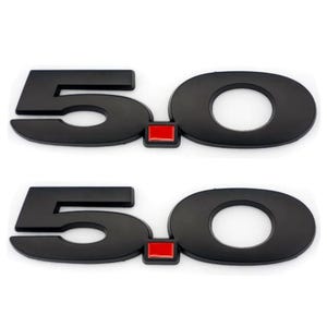 May include: Two black 5.0 emblems with a red square in the middle. The emblems are for a car.