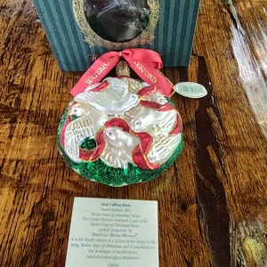 May include: A white glass Christmas ornament with four white doves and red ribbons. The ornament is part of the "Twelve Days of Christmas" series, created exclusively by Waterford. The ornament is hand-decorated and measures 11.84 cm in diameter.