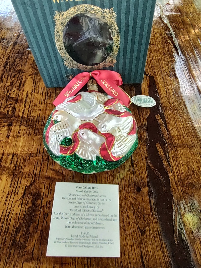 May include: A white glass Christmas ornament with four white doves and red ribbons. The ornament is part of the "Twelve Days of Christmas" series, created exclusively by Waterford. The ornament is hand-decorated and measures 11.84 cm in diameter.