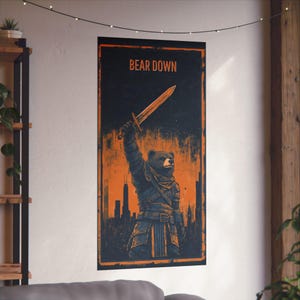 Puede incluir: Póster rectangular con un oso guerrero sosteniendo una espada, sobre un paisaje urbano. El texto "BEAR DOWN" está en la parte superior. La combinación de colores es naranja y negro. El póster está montado en una pared blanca.