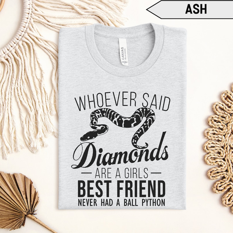 Pu&ograve; includere: Una maglietta grigia con il testo "Whoever said diamonds are a girls best friend never had a ball python" e un'illustrazione in bianco e nero di un serpente.