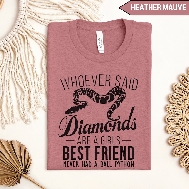 Pu&ograve; includere: Una maglietta color malva chiaro con una grafica nera che dice "Whoever said diamonds are a girls best friend never had a ball python".