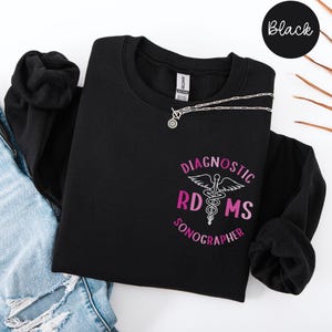 Könnte beinhalten: Schwarzer Pullover mit einer pinkfarbenen und weißen Grafik, auf der "Diagnostic RDMS Sonographer" steht.