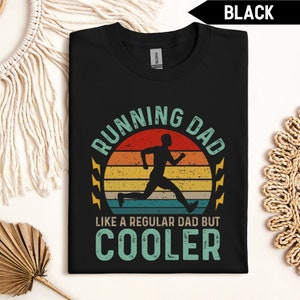 Könnte beinhalten: Schwarzes T-Shirt mit einer Grafik im Vintage-Stil von einer laufenden Person vor einem Sonnenuntergang. Der Text "Running Dad Like a Regular Dad But Cooler" ist unter der Grafik gedruckt.