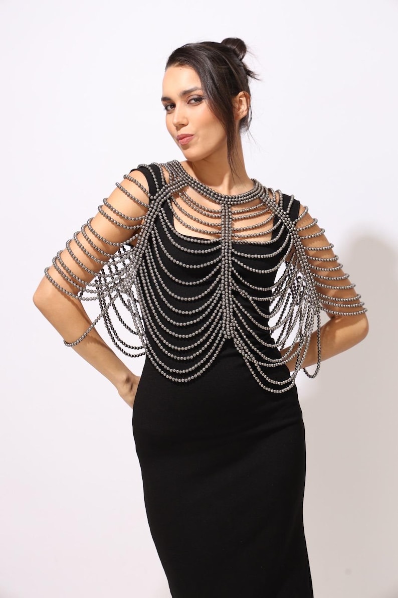 Model wearing a Metallic grey shoulder cape with cascading strands and sculptural drape over a black dress. This handmade capelet adds a bold, gothic touch to bridal, evening, or fashion looks.