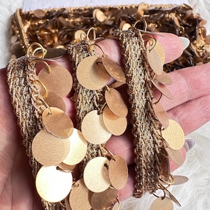 May include: Gold trim with round, dangling sequins. The trim is woven with a delicate, textured pattern.