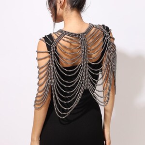 Model wearing a gunmetal beaded shoulder cape with cascading strands and sculptural drape over a black dress. This handmade capelet adds a bold, gothic touch to bridal, evening, or fashion looks.