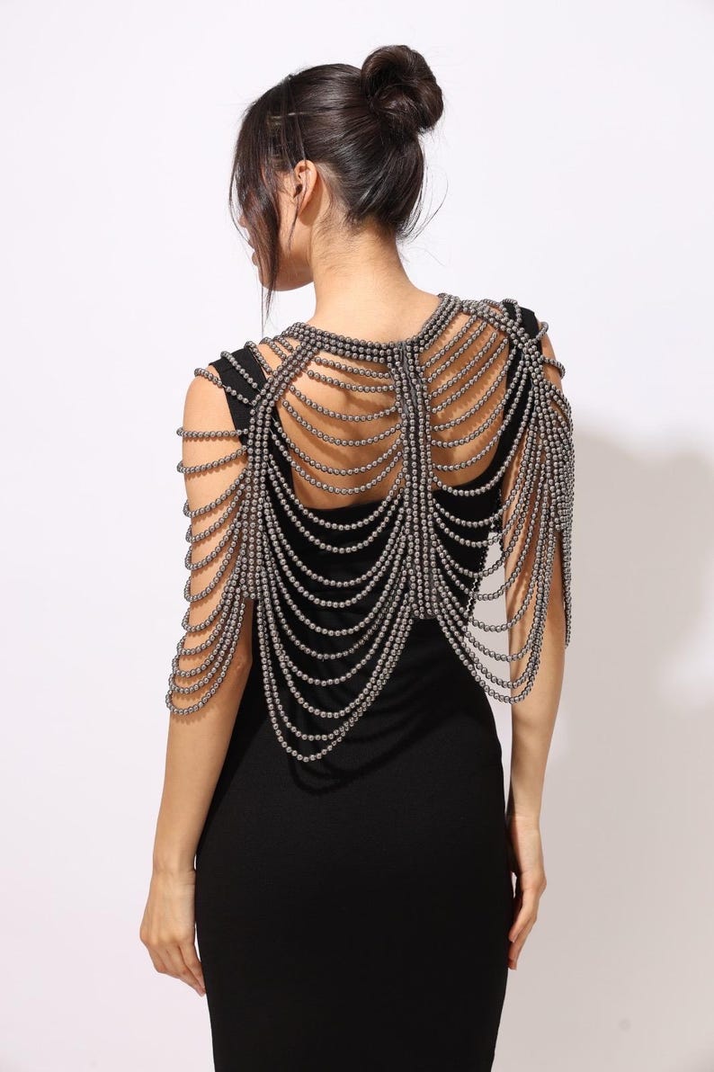 Model wearing a gunmetal beaded shoulder cape with cascading strands and sculptural drape over a black dress. This handmade capelet adds a bold, gothic touch to bridal, evening, or fashion looks.
