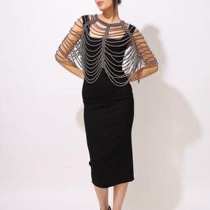 Model wearing a gunmetal beaded shoulder cape with cascading strands and sculptural drape over a black dress. This handmade capelet adds a bold, gothic touch to bridal, evening, or fashion looks.