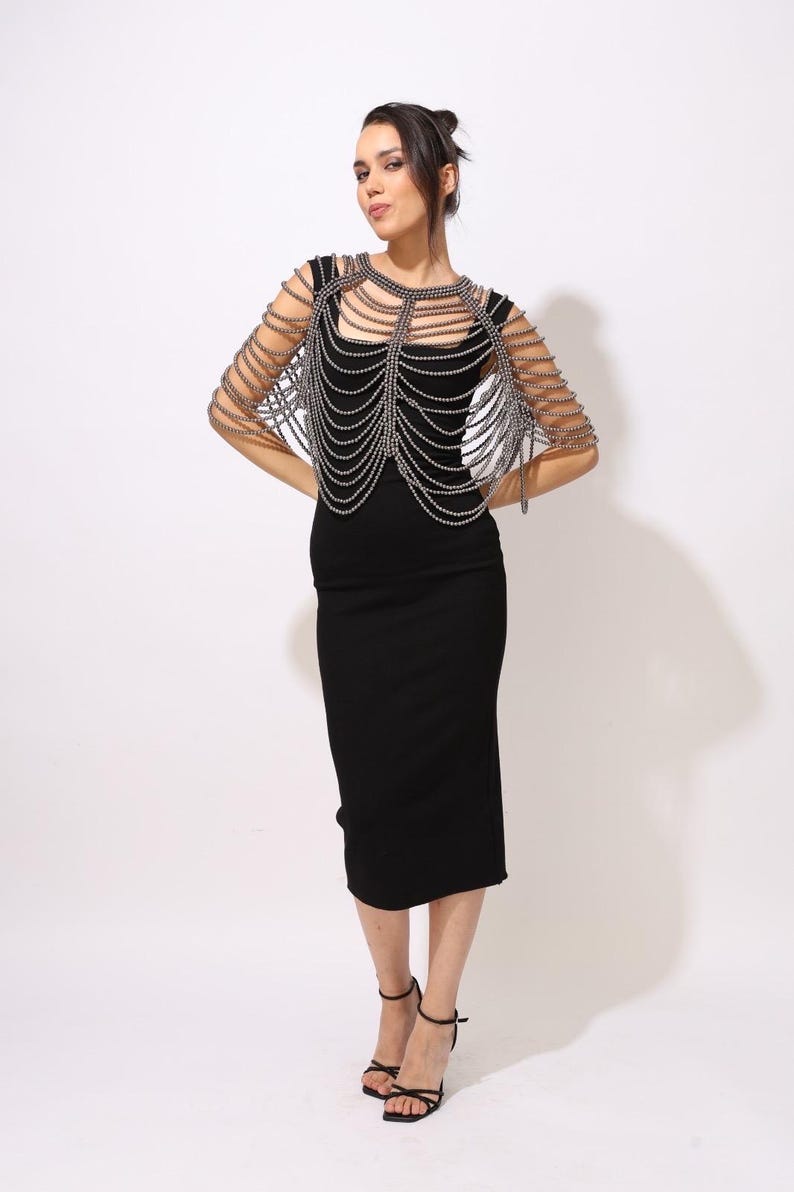 Model wearing a gunmetal beaded shoulder cape with cascading strands and sculptural drape over a black dress. This handmade capelet adds a bold, gothic touch to bridal, evening, or fashion looks.