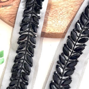May include: Black beaded trim with leaf-shaped embellishments on a sheer white fabric. The trim is perfect for adding a touch of elegance to any project.