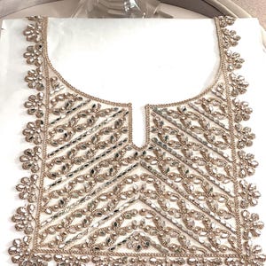 Peut inclure: Un col de vêtement blanc avec une broderie complexe en or et argent, présentant un motif géométrique de perles miroir.