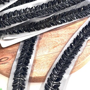 May include: Black beaded trim with a leaf design on a sheer mesh fabric. The trim is approximately 1 inch wide.