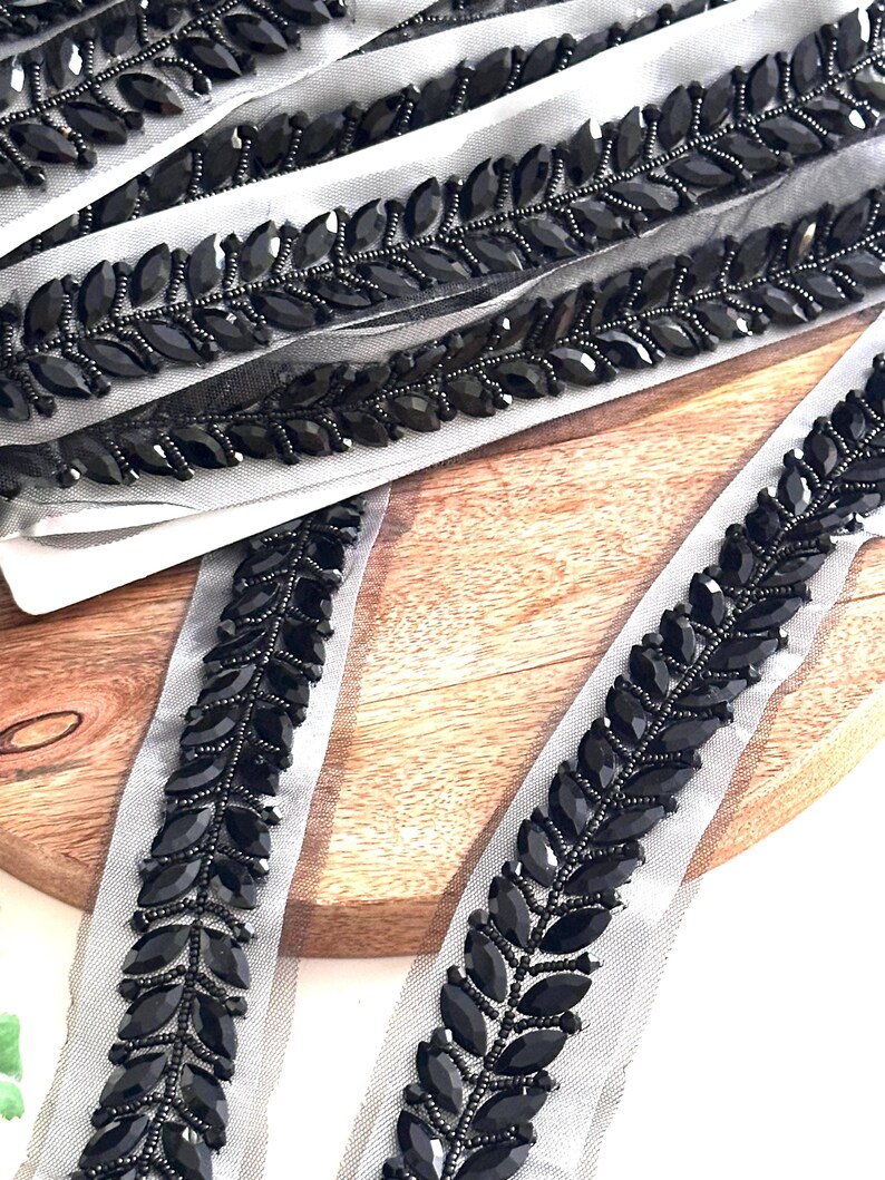 May include: Black beaded trim with a leaf design on a sheer mesh fabric. The trim is approximately 1 inch wide.